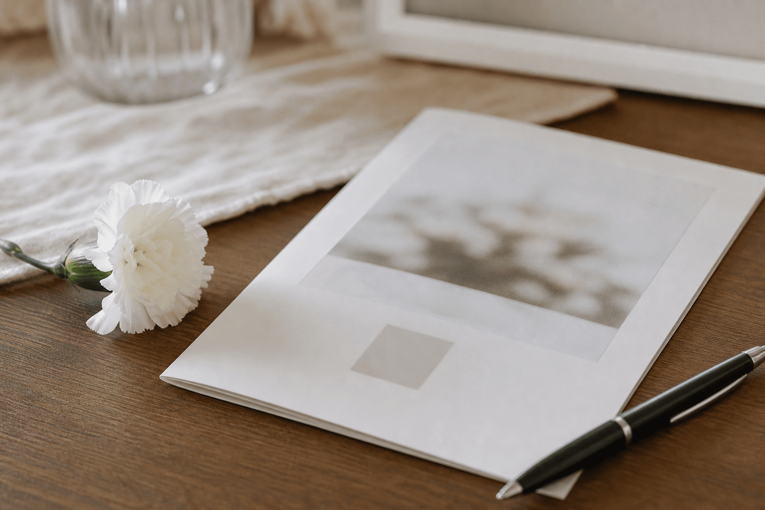 A printed memorial card and order of service program on a table with a white flower and a sign-in pen in soft natural light