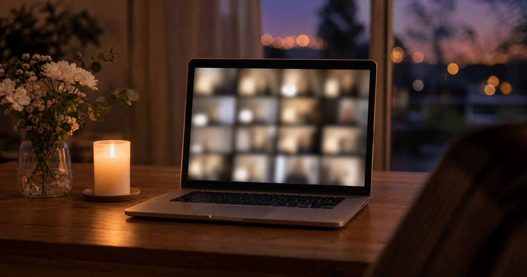 A quiet room at dusk with a laptop open on a table showing a soft, abstract grid of video call windows, beside a single lit candle
